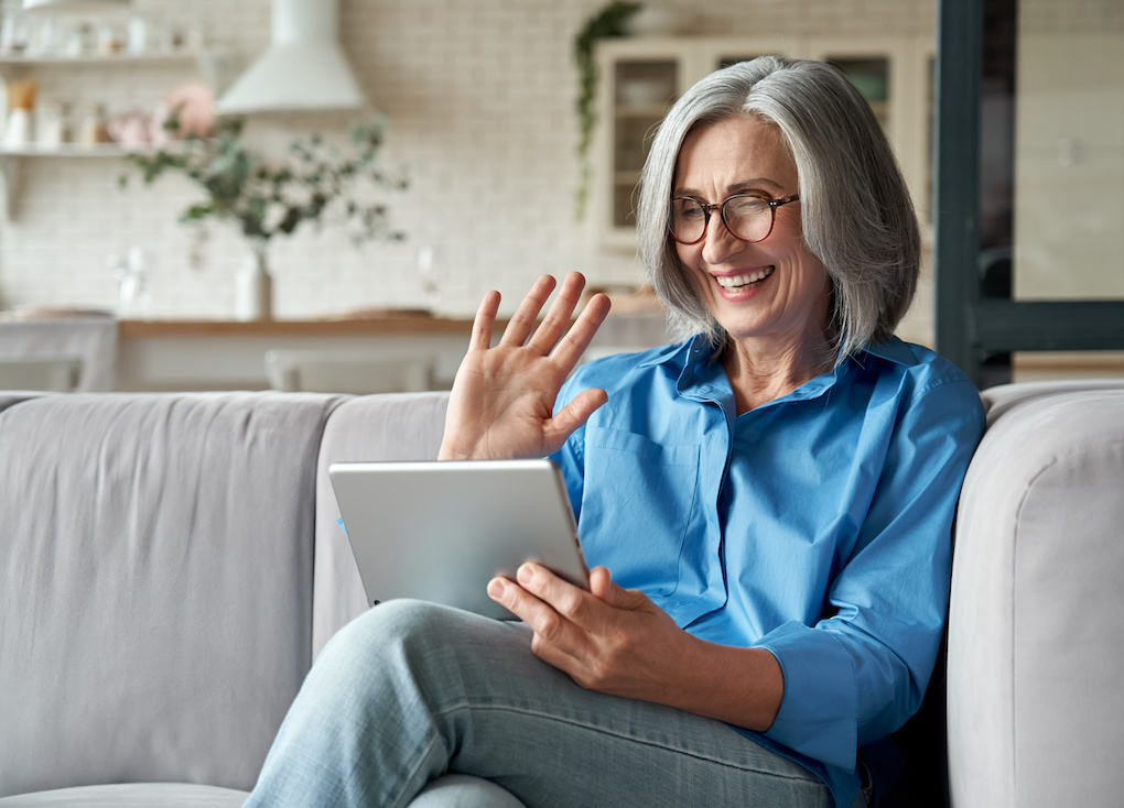 Happy older mature middle aged adult woman waving hand holding digital tablet while video calling 